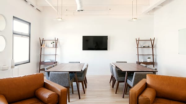 A small unmarked meeting room with a single table, four chairs and a closed blind over the window