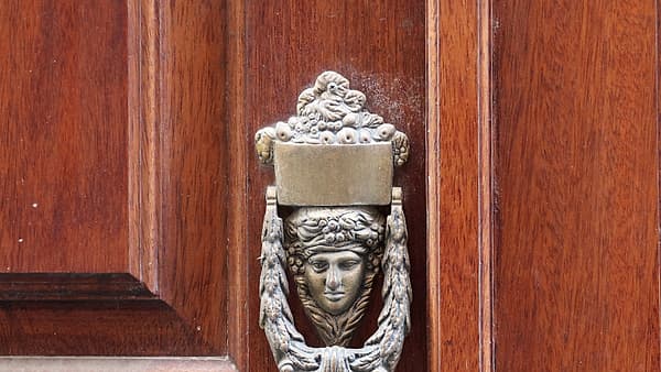 An apartment door standing slightly ajar with a loose chain lock hanging down and a keyring left hanging in the outside lock.