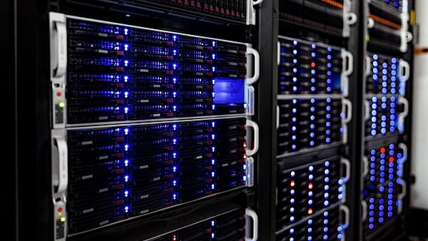 A server rack behind a glass door in a quiet windowless room, rows of small green status lights reflected in the panel