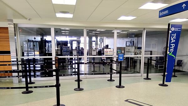 An airport arrivals hall at a quiet hour, a rope barrier drawn across one lane and a single closed booth beyond it