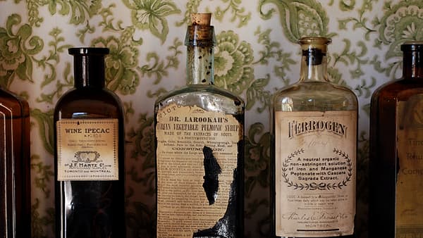 A pharmacy shelf lined with amber glass bottles of different heights, one tipped forward under a narrow strip light.
