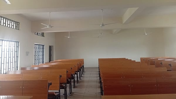 An empty classroom desk beside a window, a chair pushed back at an angle, morning light across the laminate surface