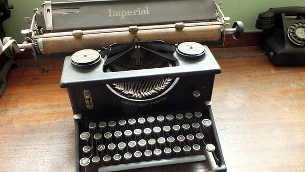 A stack of typed pages under a low desk lamp beside a stapler, a coffee cup and a pen laid across the top sheet