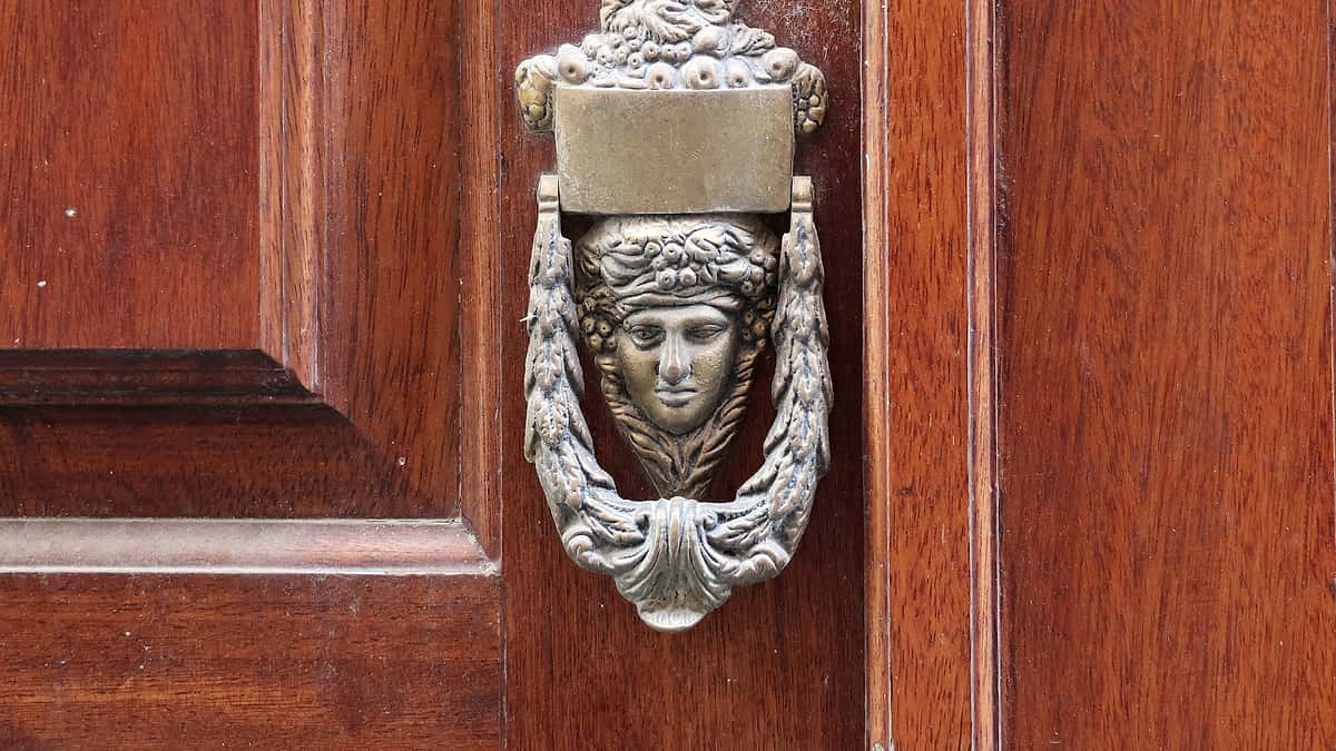 An apartment door standing slightly ajar with a loose chain lock hanging down and a keyring left hanging in the outside lock.