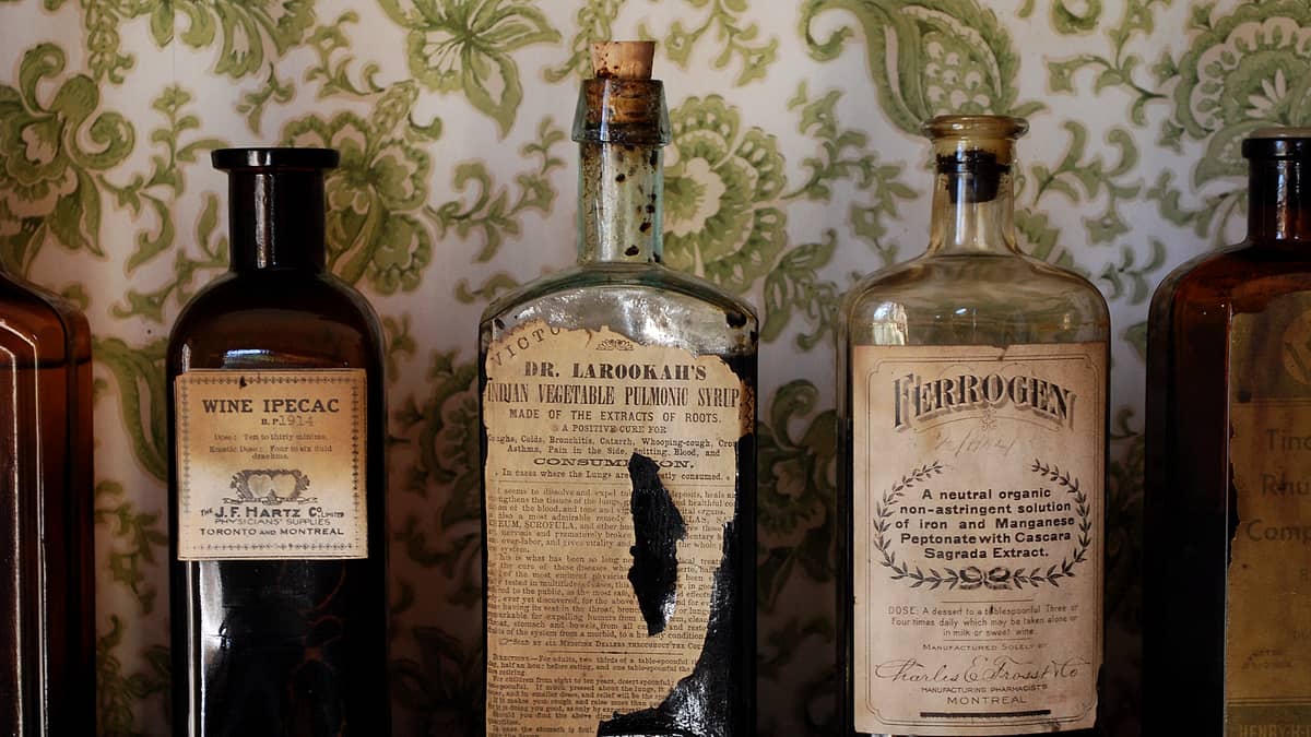 A pharmacy shelf lined with amber glass bottles of different heights, one tipped forward under a narrow strip light.
